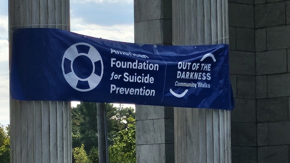 a sign for the Out of the Darkness Community Walk is wrapped around the granite columns of a monument at Roger Williams Park