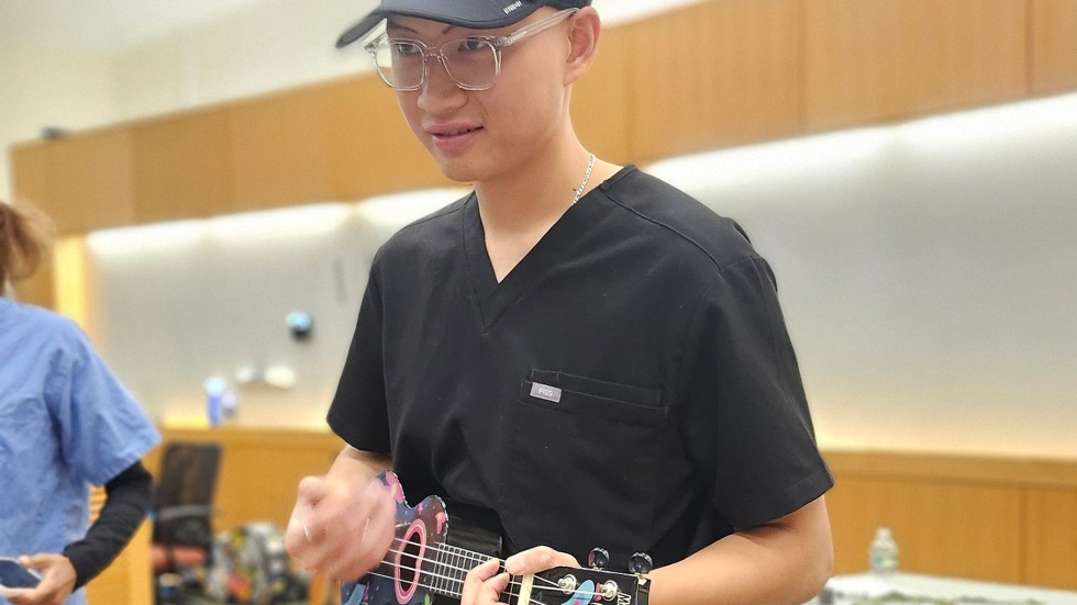 student in scrubs strums a ukulele